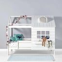 White wooden house-themed children's bed with a small roof, window, and railing. Decorated with fairy lights, cushions, and a plush bunny.