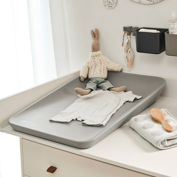 Gray changing table with a doll and baby care items on a white surface