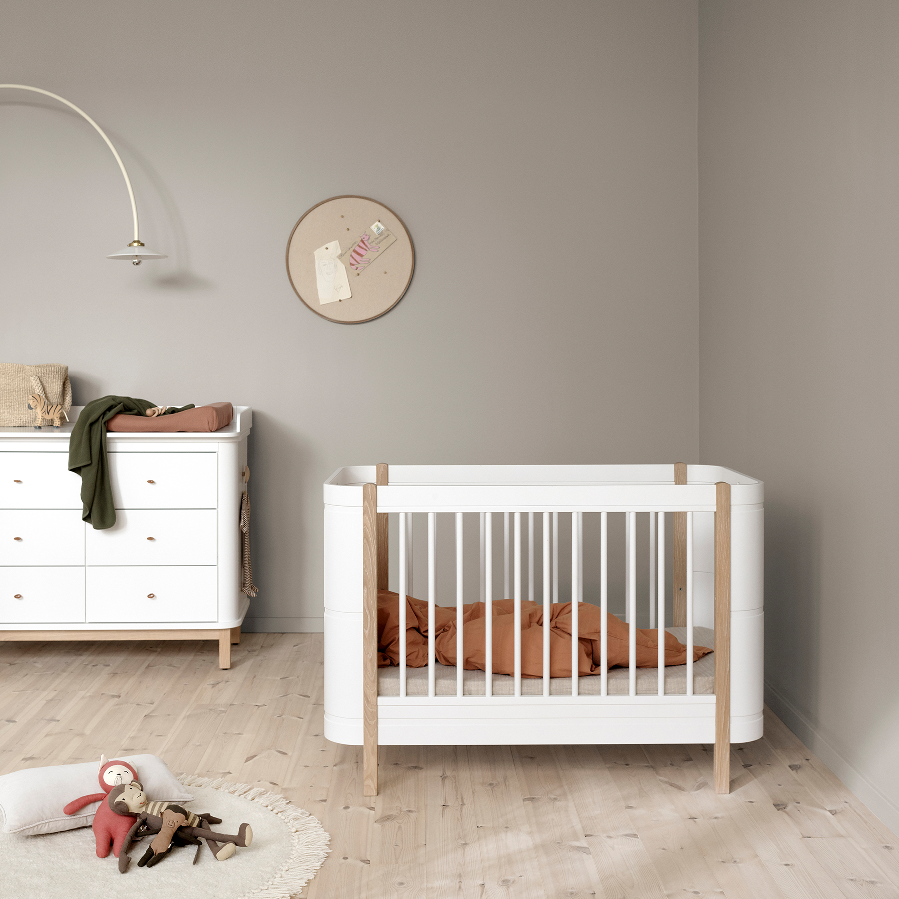 Nursery room with a white crib, dresser, and toys on a wooden floor.