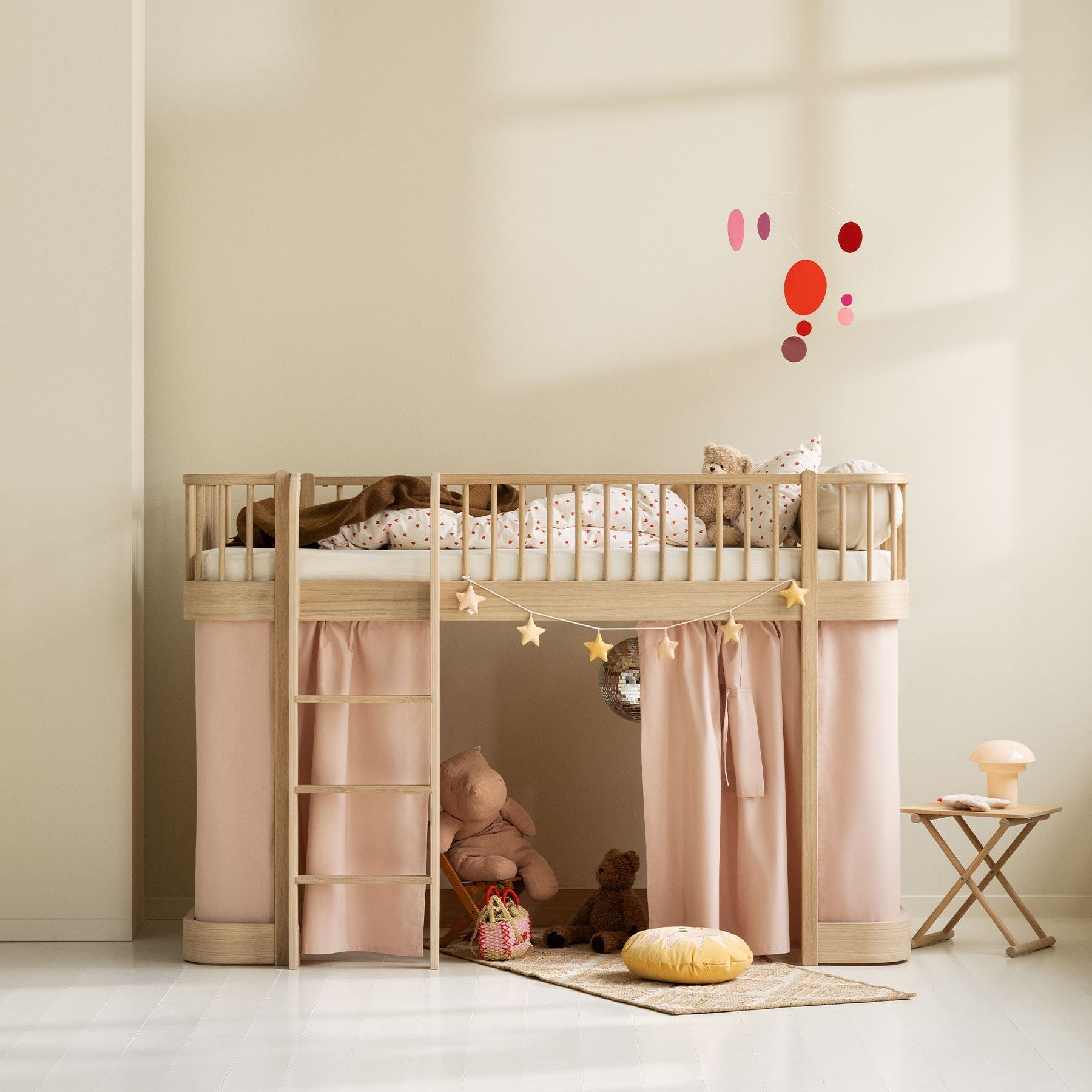 Children's room with a wooden loft bed, pink curtains, and toys on a light floor.