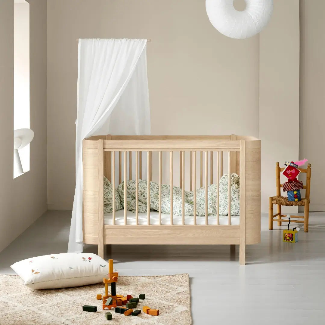 Wooden cot in a minimalistic room with toys and a chair.