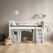 A white wooden loft bed with a ladder, dressed in neutral bedding, set in a child's bedroom with a beige wall, light wood herringbone floor, and a gray fabric play tent underneath.